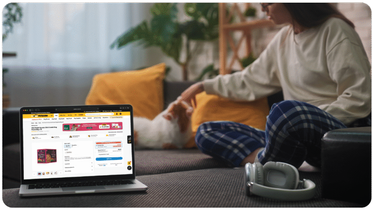 A pet parent shopping for pet food online while relaxing at home, with a dog nearby — representing common questions about digital pet shopping and PetAds retail media.